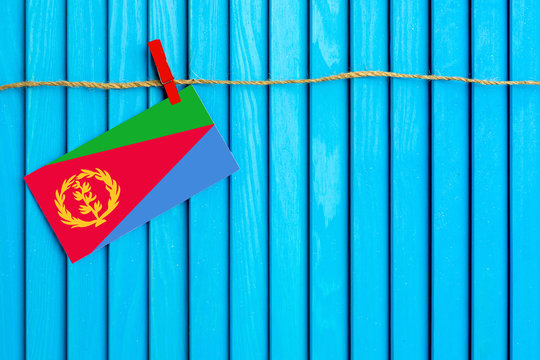 Flag of Eritrea hanging on clothesline attached with wooden clothespins on aqua blue wooden background. National day concept.