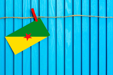 Flag of French Guiana hanging on clothesline attached with wooden clothespins on aqua blue wooden background. National day concept.