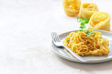 Pumpkin alfredo fettucine pasta in a ceramic plate on white background with fresh raw butternut squash slices. Autumn meal for lunch.Butternut squash recipe.Space for copy and text.Fettuccine pasta