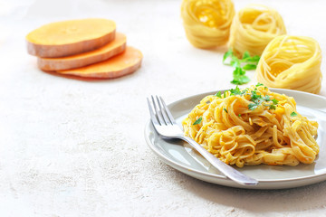 Pumpkin alfredo fettucine pasta in a ceramic plate on white background with fresh raw butternut squash slices. Autumn meal for lunch.Butternut squash recipe.Space for copy and text.Fettuccine pasta