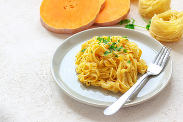 Pumpkin alfredo fettucine pasta in a ceramic plate on white background with fresh raw butternut squash slices. Autumn meal for lunch.Butternut squash recipe.Space for copy and text.Fettuccine pasta