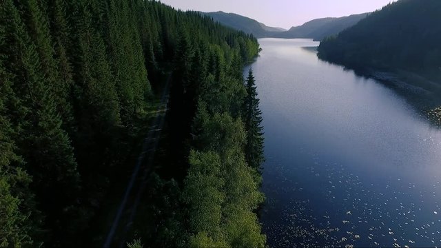 Aerial of dirt road running parallel with lake in beautiful Norwegian landscape