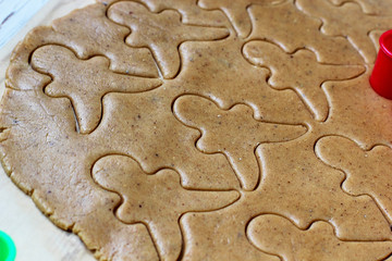 process of dealing with gingerbread man cookies,use red gingerbread man  mold cutting gingerbread dough on baking paper around colorful cookie cutters on white wooden table.top view