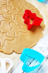 process of dealing with gingerbread man cookies,use red gingerbread man  mold cutting gingerbread dough on baking paper around colorful cookie cutters on white wooden table.top view