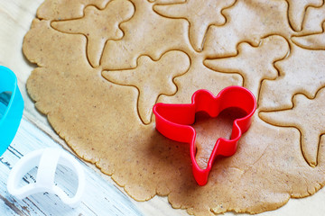 process of dealing with gingerbread man cookies,use red gingerbread man  mold cutting gingerbread dough on baking paper around colorful cookie cutters on white wooden table.top view