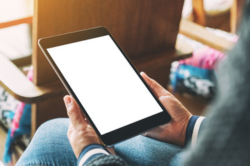 Mockup image of a woman holding black tablet with blank white desktop screen while sitting on wooden chair