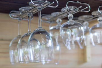 Clean empty wine glasses in row hang on shelf bar in light sunshine