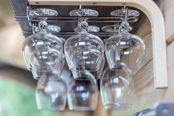 Clean empty cognac glasses in row hang on shelf bar in light sunshine