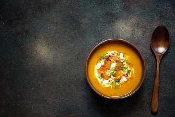 Roasted pumpkin and carrot soup with cream, seeds and fresh green in ceramic bowl on grunge black background. Top view.Spaces for text and copy