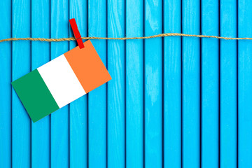 Flag of Ireland hanging on clothesline attached with wooden clothespins on aqua blue wooden background. National day concept.