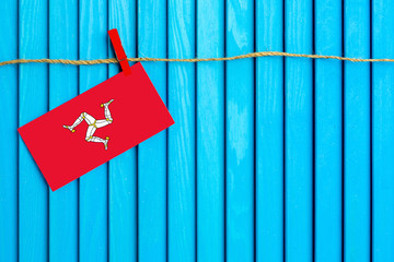 Flag of Isle Of Man hanging on clothesline attached with wooden clothespins on aqua blue wooden background. National day concept.
