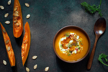 Roasted pumpkin and carrot soup with cream, seeds and fresh green in ceramic bowl on grunge black background. Top view.Spaces for text and copy