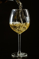 White wine being poured in a wine glass on a dark background