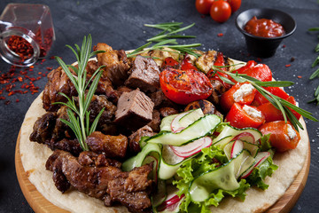 Close up view on tasty grilled meat with vegetables on georgian pita. shashlik or barbecue meat on pita. Shish kebab, traditional georgian cuisine food. Copy space for design. Dark background