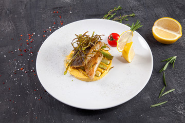 Close up view on grilled tasty seabass fillet with asparagus and lemon on white plate. Dark background. Restaurant style food photo background. Ready to eat Seafood fish