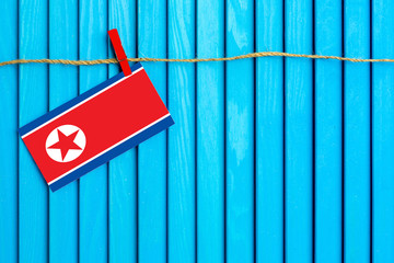 Flag of North Korea hanging on clothesline attached with wooden clothespins on aqua blue wooden background. National day concept.