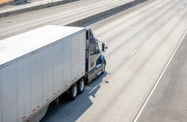 Dark big rig semi truck transporting cargo in dry van semi trailer running on wide multiline...