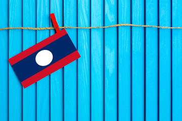 Flag of Laos hanging on clothesline attached with wooden clothespins on aqua blue wooden background. National day concept.