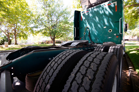 Rear tires tread of a green big rig semi truck parked on a street under the trees