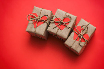 Romantic presents set. Gift boxes wrapped in brown craft paper and tie hemp string. Carton hearts. Red solid background. Delivered parcels. 