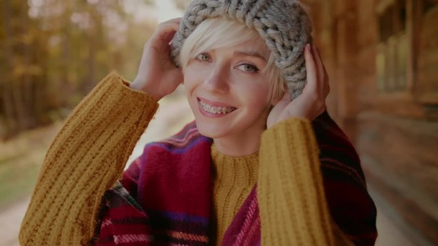 Happy smiling hipster girl with braces on her teeth plays with knitted beanie hat, hides her eyes