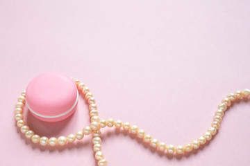 Cosmetic cream and string of pearls on pink with place for text. Beauty, makeup, femininity, fashion concept