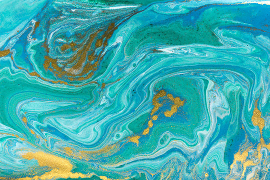 Liquid uneven blue and green marbling pattern with golden glitter and glare of light.