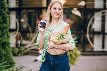 Beautiful blonde girl holds package with food in her hands. Beautiful blonde drinking coffee.