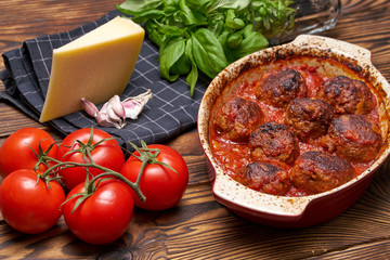 Meatballs in tomato saucel. rustic table. ceramice bowl. black napkin with white cage. piece of hard cheese, fresh basel, garlic