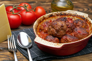 Meatballs cooked with tomato sauce in white and red casserole on wooden rustic table, with...