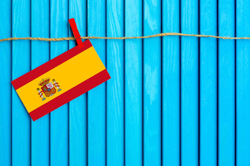 Flag of Spain hanging on clothesline attached with wooden clothespins on aqua blue wooden background. National day concept.