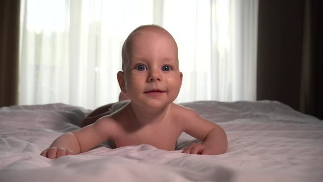 Portrait. Cute Little Happy Baby boy laying on white bed sheet. 4K