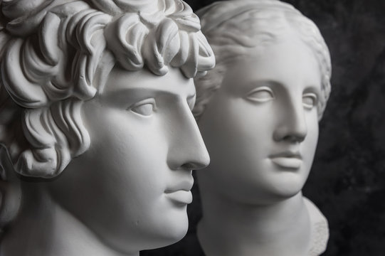 Gypsum copy of ancient statue Antinous and Venus head on dark textured background. Plaster sculpture face.