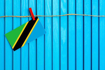 Flag of Tanzania hanging on clothesline attached with wooden clothespins on aqua blue wooden background. National day concept.
