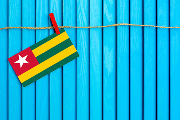 Flag of Togo hanging on clothesline attached with wooden clothespins on aqua blue wooden background. National day concept.