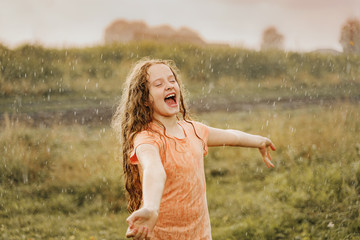 Laughing child spread its arms and catches raindrops. Freedom, happy childhood, healthy lifestyle concept.