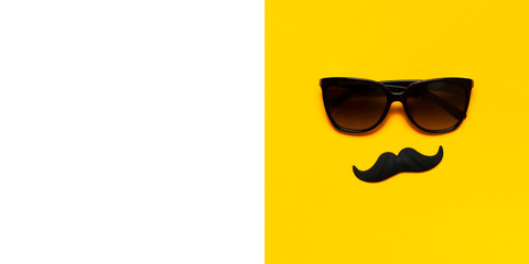 Creative party decoration concept. Black mustache, sunglasses, props for photo booths, carnival parties on yellow background top view flat lay copy space. Father's day Men's health awareness month