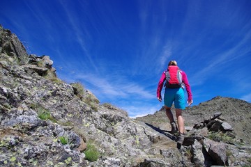 Fototapeta premium Jeune femme qui grimpe t marche en montagne avec ciel bleu et sac à dos
