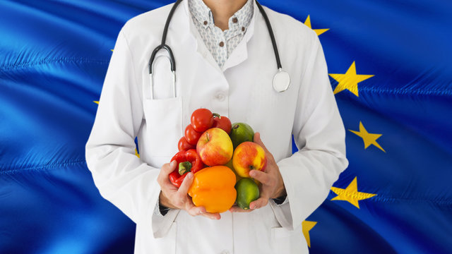 Doctor is holding fruits and vegetables in hands with European Union flag background. National healthcare concept, medical theme.