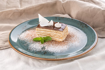 Vanilla cake with chocolate icing thin layers of biscuit on blue plate on tablecloth