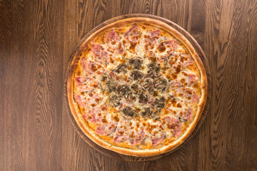 Italian Pizza with ham, sliced mushrooms, tomato sauce and cheddar isolated on wooden background