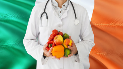 Doctor is holding fruits and vegetables in hands with Ireland flag background. National healthcare concept, medical theme.