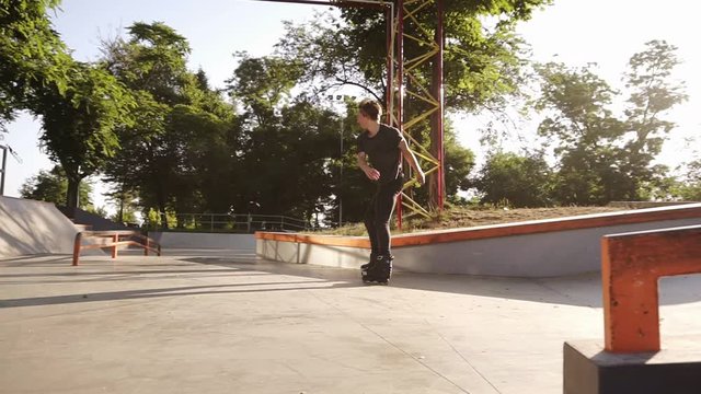 A young athlete performs a trick on rollers - jumps through the railings, doing 360 degrees turn and bend his legs in the air. Slow motion. Outdoors skate park