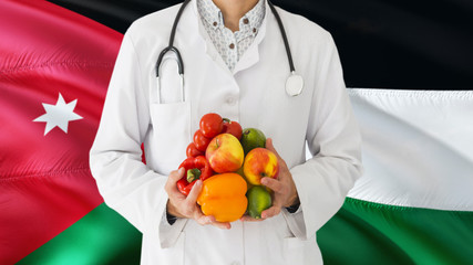 Doctor is holding fruits and vegetables in hands with Jordan flag background. National healthcare concept, medical theme.