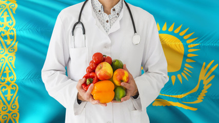 Doctor is holding fruits and vegetables in hands with Kazakhstan flag background. National healthcare concept, medical theme.