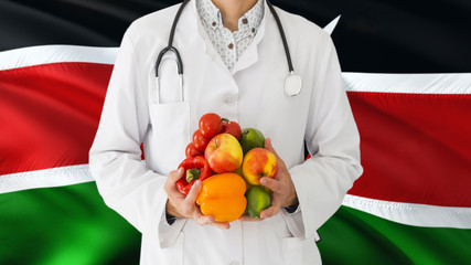 Doctor is holding fruits and vegetables in hands with Kenya flag background. National healthcare concept, medical theme.