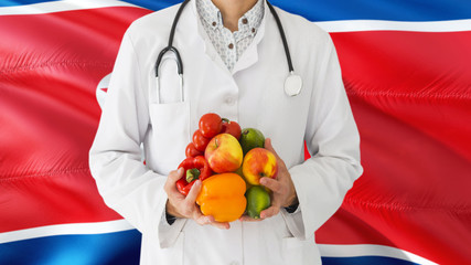 Doctor is holding fruits and vegetables in hands with North Korea flag background. National healthcare concept, medical theme.