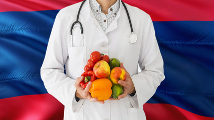 Doctor is holding fruits and vegetables in hands with Laos flag background. National healthcare concept, medical theme.