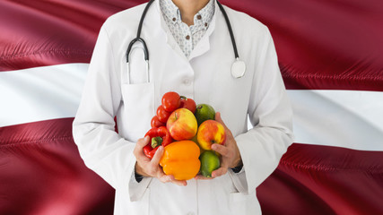 Doctor is holding fruits and vegetables in hands with Latvia flag background. National healthcare concept, medical theme.