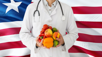 Doctor is holding fruits and vegetables in hands with Liberia flag background. National healthcare concept, medical theme.